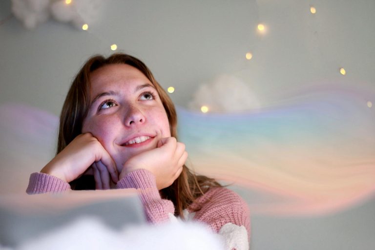 A smiling teenager gazes thoughtfully upwards with a dreamy rainbow overlay, creating a whimsical portrait.