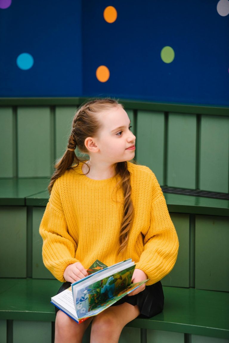 A young girl sits reading a book in a vibrant, playful setting indoors.
