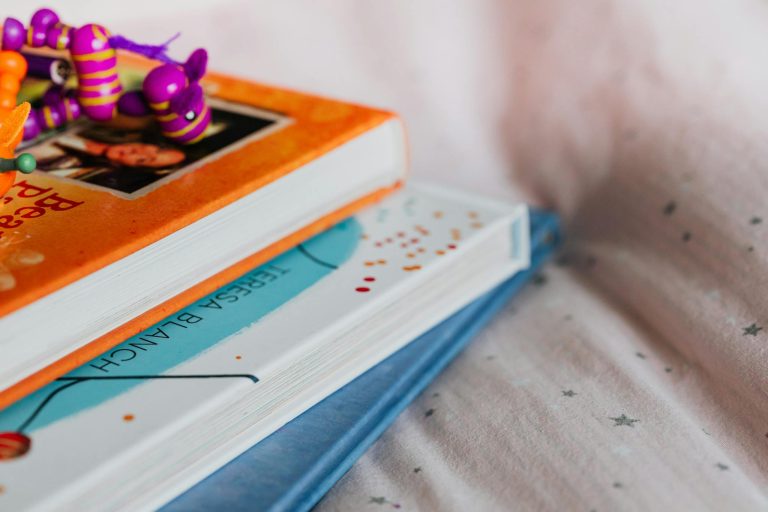 Close-up of colorful children's books stacked with a playful toy on top indoors.